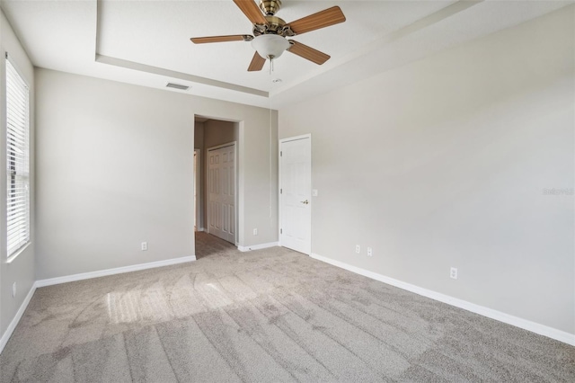 empty room with ceiling fan, a raised ceiling, and light carpet