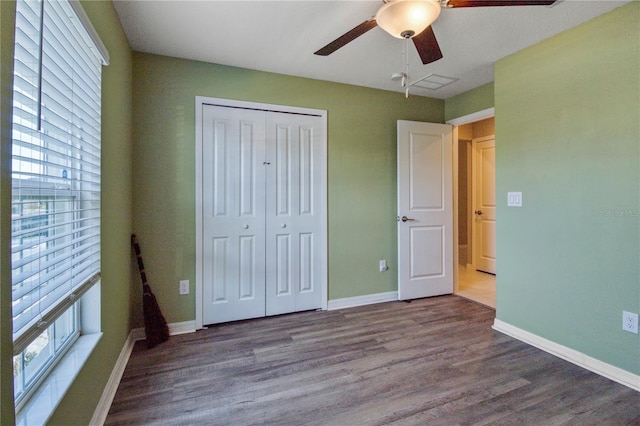 unfurnished bedroom featuring ceiling fan, wood-type flooring, multiple windows, and a closet