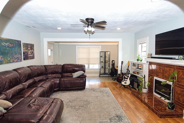 living room featuring a textured ceiling, light wood-type flooring, a wealth of natural light, and ceiling fan