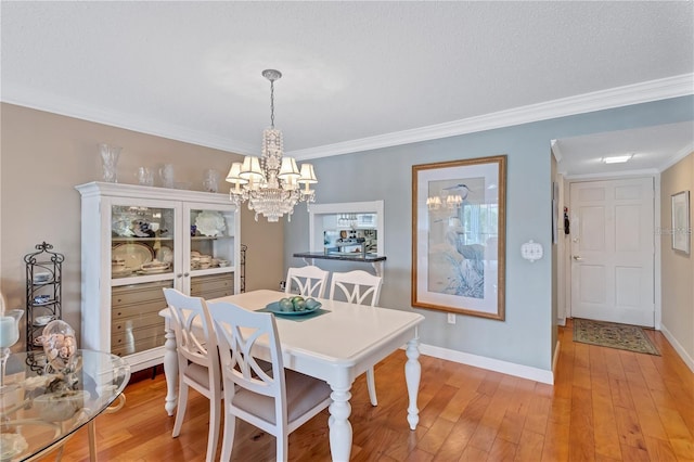 dining space with a chandelier, a textured ceiling, light wood-type flooring, and crown molding