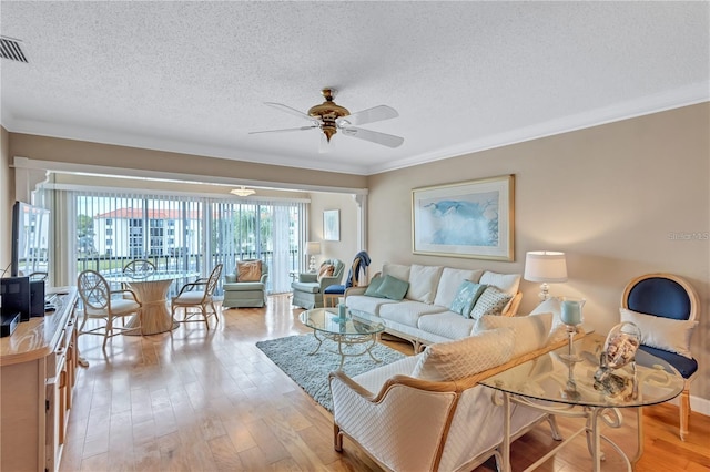 living room with ceiling fan, light wood-type flooring, a textured ceiling, and ornamental molding