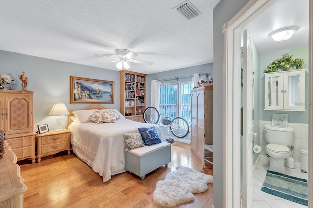 bedroom featuring a textured ceiling, ensuite bath, light hardwood / wood-style flooring, and ceiling fan