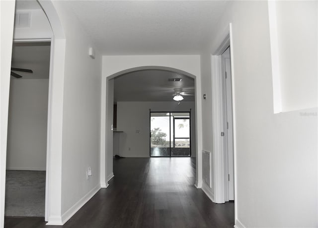 corridor with arched walkways, dark wood-style flooring, visible vents, and baseboards