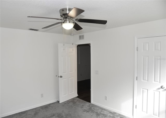 unfurnished bedroom featuring a textured ceiling, dark carpet, and ceiling fan