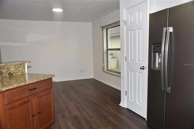 kitchen featuring stainless steel fridge, baseboards, brown cabinetry, dark wood finished floors, and light stone counters