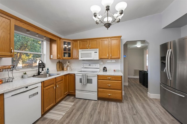 kitchen featuring white appliances, arched walkways, brown cabinetry, vaulted ceiling, and a sink