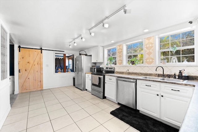 kitchen with appliances with stainless steel finishes, white cabinetry, sink, backsplash, and a barn door