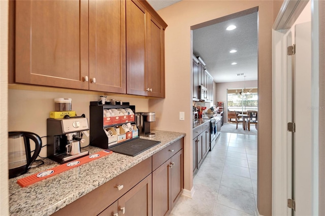 kitchen featuring light tile patterned floors, a textured ceiling, appliances with stainless steel finishes, a notable chandelier, and light stone counters