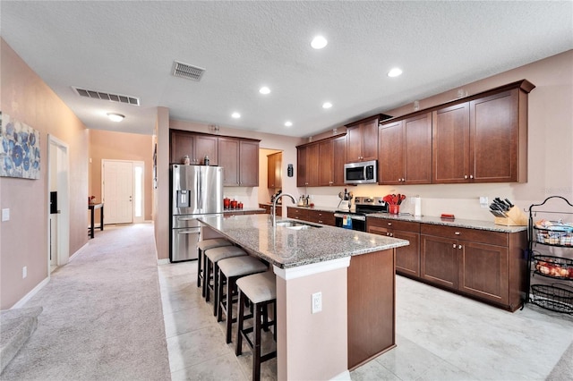 kitchen featuring a center island with sink, a kitchen breakfast bar, sink, light stone countertops, and stainless steel appliances