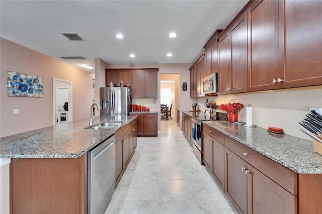 kitchen featuring a center island with sink, stone countertops, sink, and appliances with stainless steel finishes