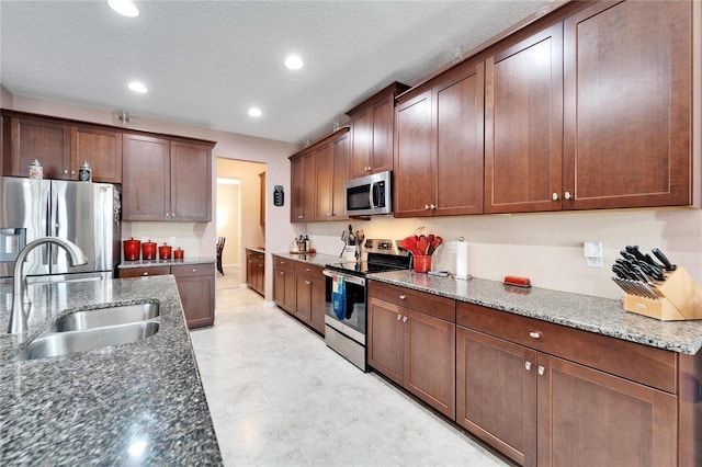 kitchen with a textured ceiling, stainless steel appliances, dark stone countertops, and sink