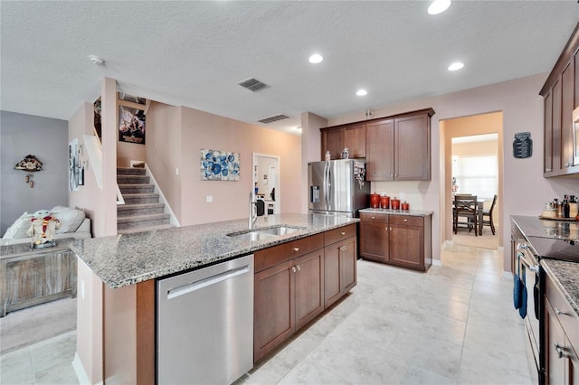 kitchen featuring sink, an island with sink, a textured ceiling, and appliances with stainless steel finishes