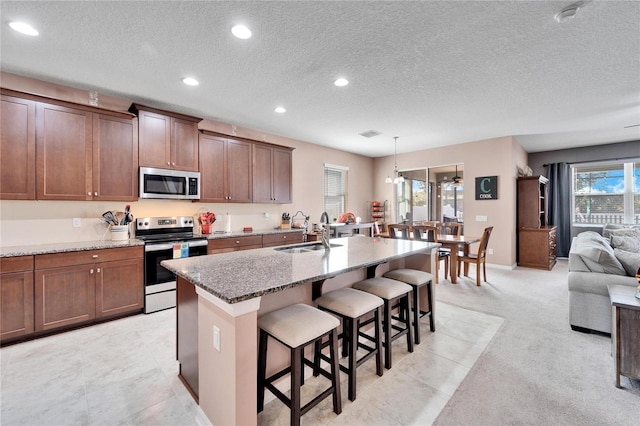 kitchen with light carpet, stainless steel appliances, sink, pendant lighting, and a center island with sink