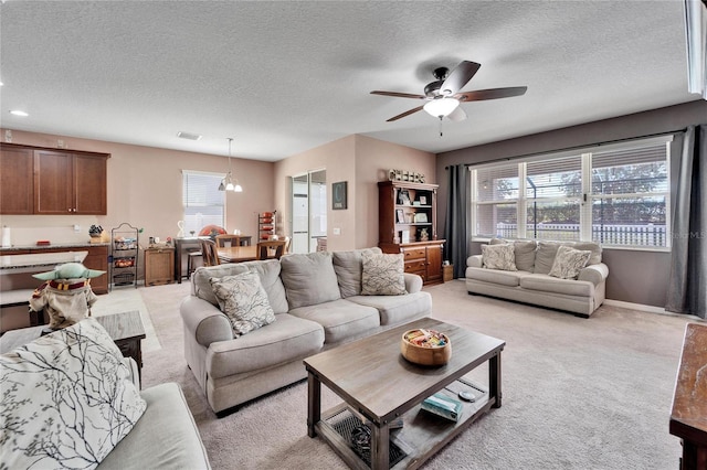 living room with ceiling fan with notable chandelier, light colored carpet, and a textured ceiling