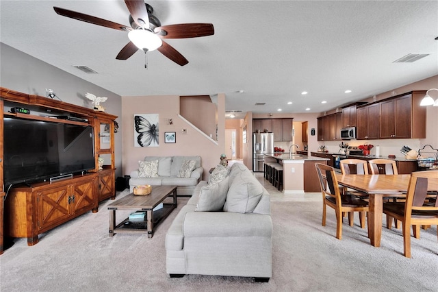 living room featuring ceiling fan, sink, light colored carpet, and a textured ceiling