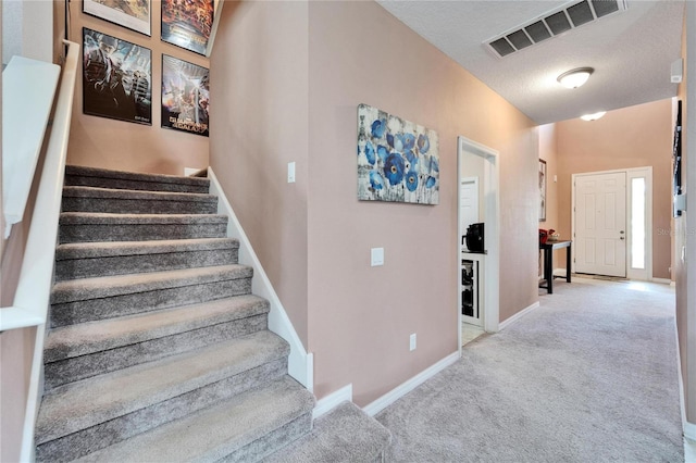 stairway with carpet floors and a textured ceiling