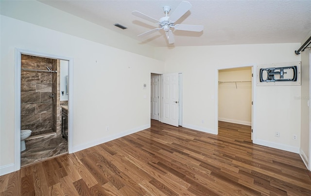 unfurnished bedroom with ceiling fan, dark hardwood / wood-style floors, ensuite bathroom, lofted ceiling, and a walk in closet