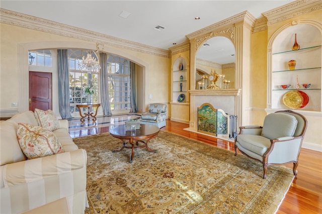 living room featuring built in shelves, crown molding, a chandelier, and light wood-type flooring