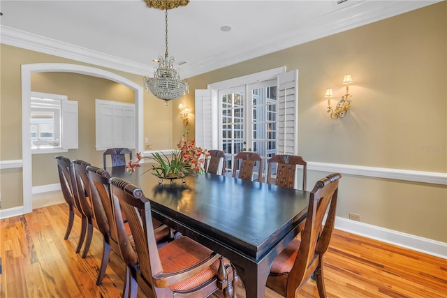 dining area with a chandelier, french doors, light wood-type flooring, and ornamental molding