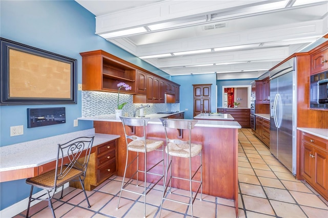 kitchen with a breakfast bar, a center island, backsplash, light tile patterned floors, and stainless steel built in refrigerator