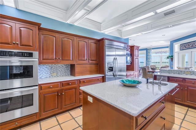 kitchen featuring sink, a kitchen island with sink, beamed ceiling, decorative backsplash, and appliances with stainless steel finishes