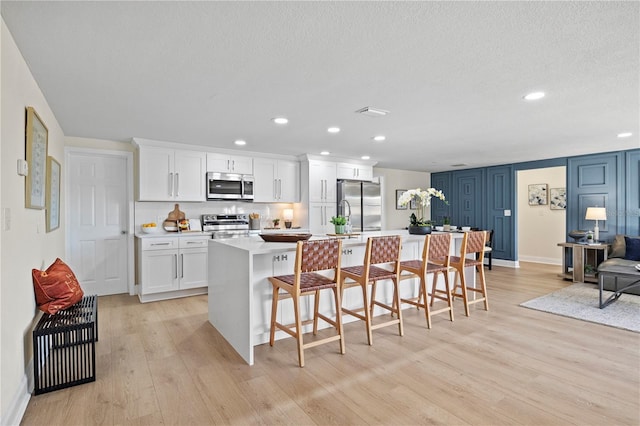 kitchen featuring appliances with stainless steel finishes, an island with sink, a kitchen bar, white cabinets, and light wood-type flooring