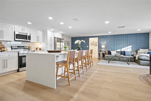 kitchen with white cabinetry, a center island, stainless steel appliances, and light wood-type flooring