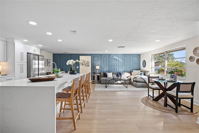 kitchen with white cabinets, a kitchen breakfast bar, light wood-type flooring, blue cabinetry, and stainless steel refrigerator