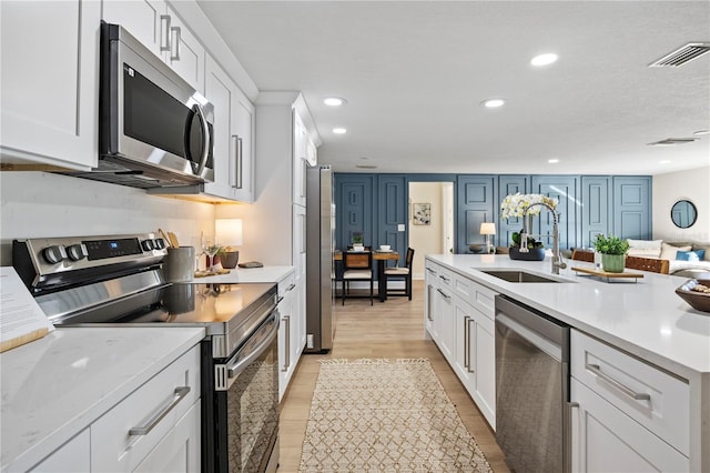 kitchen with white cabinets, appliances with stainless steel finishes, light wood-type flooring, and sink