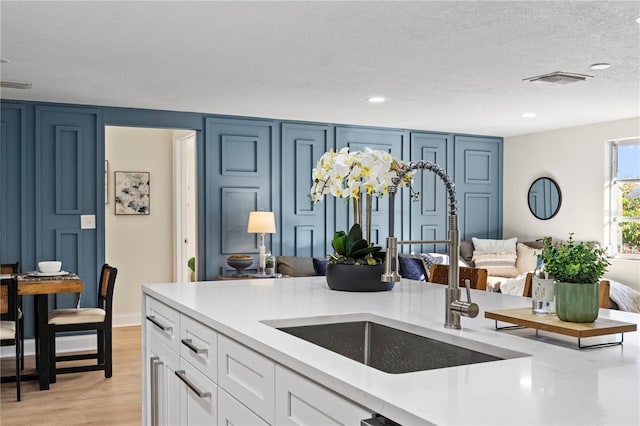 kitchen featuring sink, light wood-type flooring, a textured ceiling, blue cabinetry, and white cabinetry