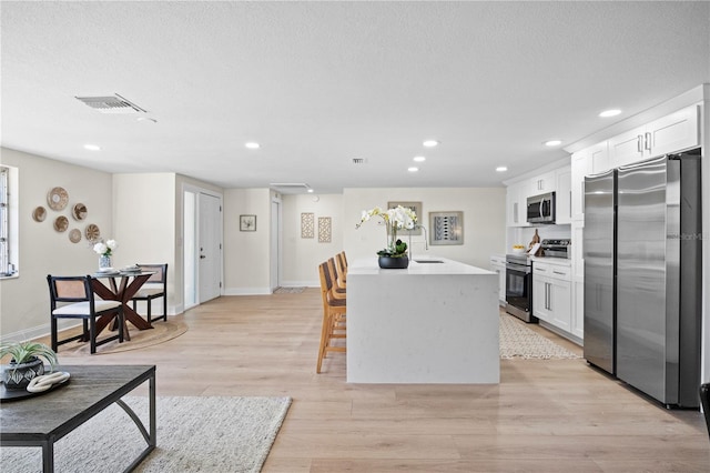 kitchen with white cabinetry, sink, appliances with stainless steel finishes, a kitchen island, and light wood-type flooring