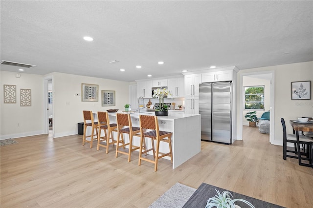 kitchen featuring white cabinetry, stainless steel appliances, a kitchen breakfast bar, a center island with sink, and light wood-type flooring