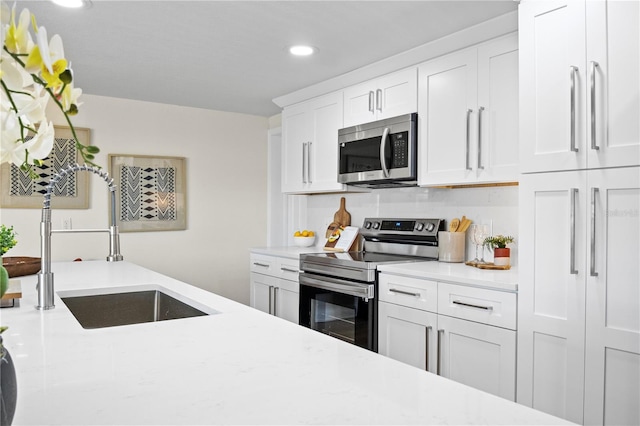 kitchen featuring light stone countertops, sink, stainless steel appliances, decorative backsplash, and white cabinets