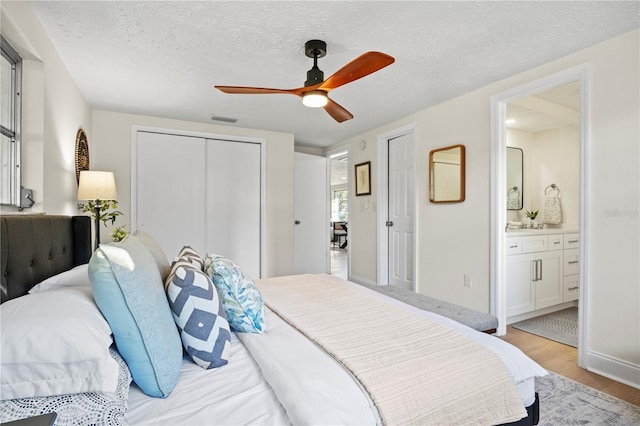 bedroom featuring ceiling fan, ensuite bathroom, a textured ceiling, a closet, and light wood-type flooring