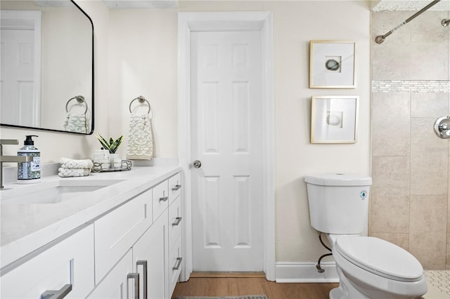 bathroom with tiled shower, toilet, vanity, and hardwood / wood-style flooring