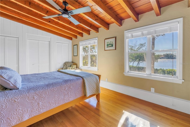 bedroom featuring light wood-type flooring, ceiling fan, lofted ceiling with beams, wooden ceiling, and multiple closets