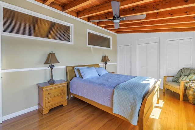 bedroom with two closets, ceiling fan, lofted ceiling with beams, wooden ceiling, and hardwood / wood-style floors