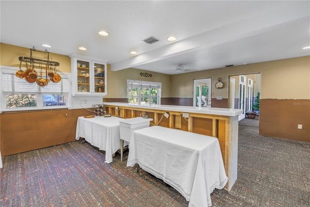 kitchen with kitchen peninsula, a kitchen bar, dark colored carpet, and beam ceiling