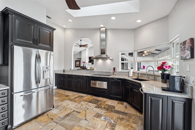 kitchen featuring wall chimney range hood, stainless steel refrigerator with ice dispenser, a ceiling fan, and a warming drawer