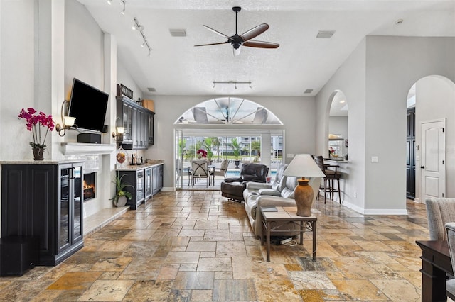 living room with rail lighting, visible vents, a ceiling fan, stone tile flooring, and a textured ceiling