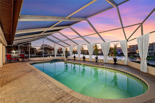 outdoor pool featuring glass enclosure, a water view, and a patio