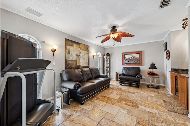living room featuring stone tile floors, visible vents, ornamental molding, a textured ceiling, and ceiling fan