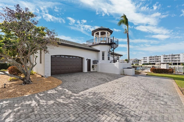 view of front facade featuring fence, a garage, a balcony, stucco siding, and decorative driveway