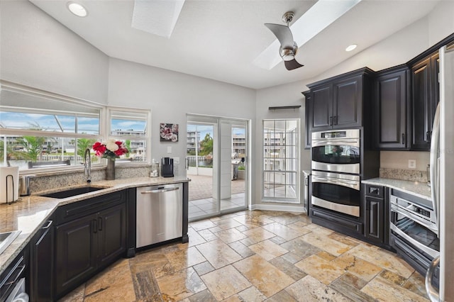 kitchen with stone tile flooring, appliances with stainless steel finishes, a sink, and a skylight