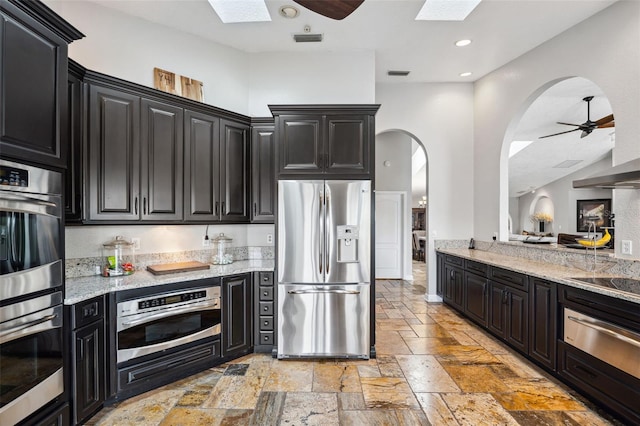 kitchen with a ceiling fan, a skylight, a warming drawer, stainless steel appliances, and dark cabinets