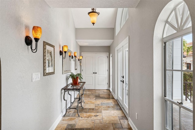 entryway with stone tile floors, a textured wall, french doors, and baseboards