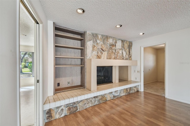 unfurnished living room featuring built in features, wood-type flooring, a tiled fireplace, and a textured ceiling