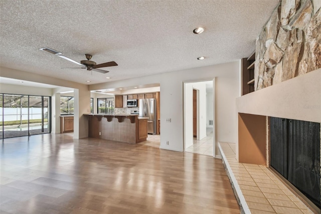 unfurnished living room with ceiling fan, light hardwood / wood-style flooring, a large fireplace, and a textured ceiling