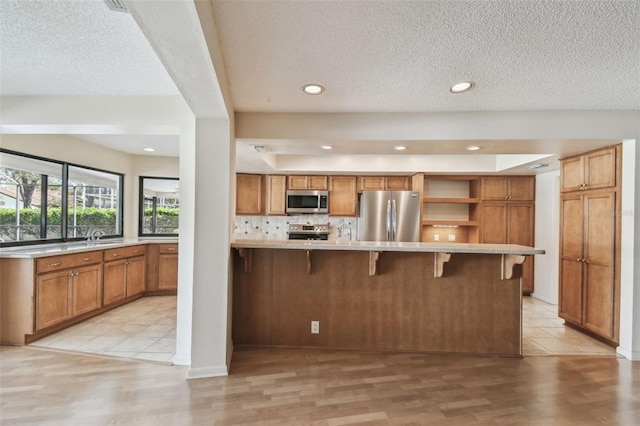 kitchen with a kitchen bar, backsplash, light wood-type flooring, and appliances with stainless steel finishes