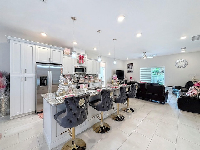 kitchen with a breakfast bar, white cabinets, appliances with stainless steel finishes, decorative light fixtures, and light stone counters